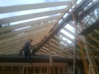 Rafters going up over a new addition with a worker on the wall in Mayville