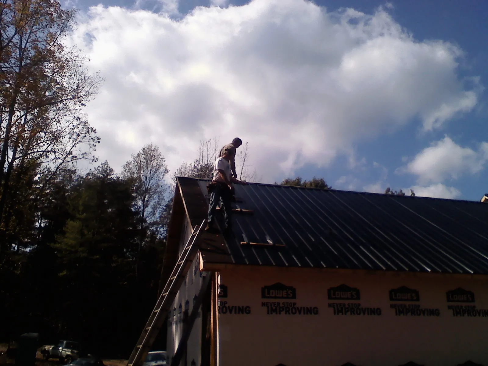 Roofer fastening dark metal panels high against a cloudy sky, from a Roof Inspection job in Mayville